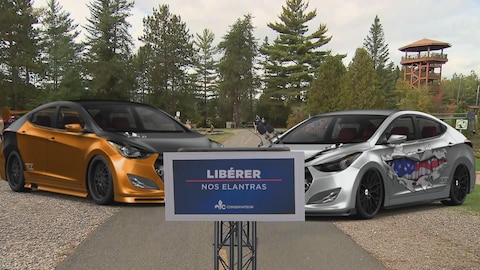 Deux voitures dans un parc avec une affiche du parti conservateur du Québec.
