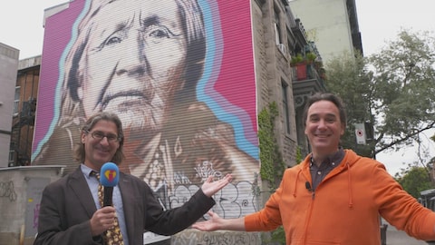 Deux personnes  posent devant la murale d'une aînée autochtone.