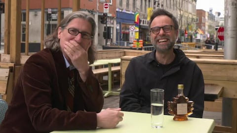 Zone 3 Jean-René Dufort et son invité sont assis sur une terrasse du Village à Montréal. Une bouteille de sirop d'érable est sur la table.