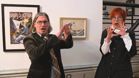Devant des tableaux dans une exposition, Chantal Lamarre et Jean-René Dufort font des triangles avec leurs mains comme le groupe Angine de poitrine.