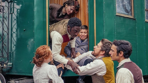 Fogg, Fix et Passepartout près d'un homme dans un train. Un enfant pleure assis par terre.