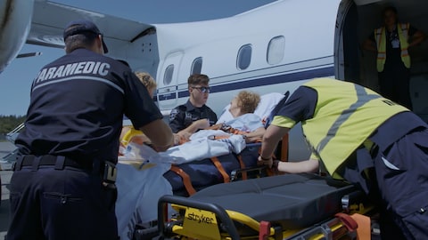 Une femme dans une civière, entourée d'ambulanciers paramédicals.