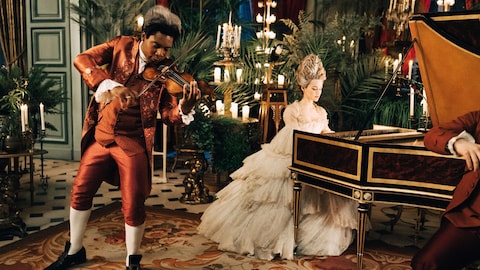 Yoli Fuller (Saint-Georges) joue du violon et Emilia Schüle (Marie Antoinette) joue du piano dans une salle de réception luxuriante.