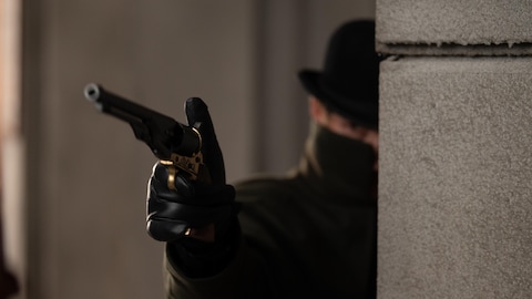 Un homme caché derrière un mur pointe un pistolet.