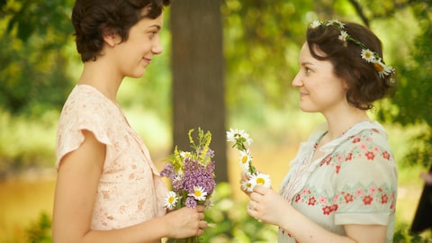 Léa et Gabrielle se regardent en tenant des fleurs dans la série Le monde de Gabrielle Roy.