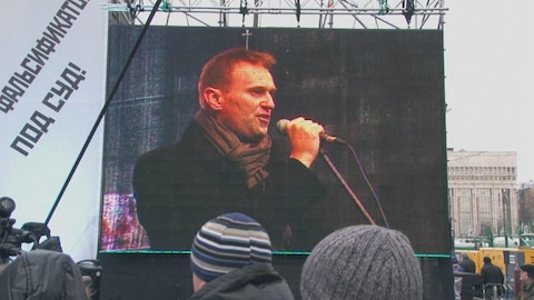 Alexeï Navalny, politicien russe, qu'on voit tenant un micro sur un écran géant dans un lieu public.