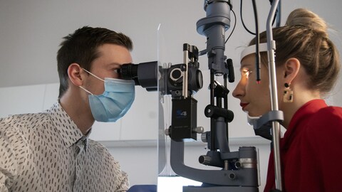 Un optométriste examine l'oeil d'une jeune femme avec l'aide d'un appareil spécialisé.