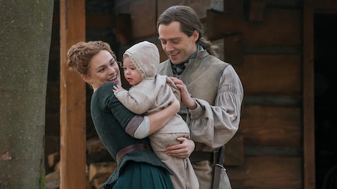 Brianna qui prend son bébé dans ses bras et Roger qui les regarde heureux.