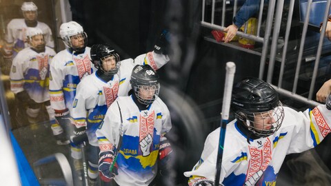 Quatre joueurs ukrainiens pee-wee s'avancent vers la glace. Un spectateur tend la main à un des joueurs, qui la lui tend en retour.