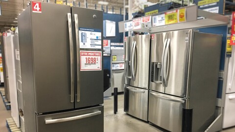 Des réfrigérateurs argentés sont présentés les uns à côté des autres dans un coin du magasin d'électroménagers. Des étiquettes rouges sont notamment apposées sur les électroménagers.