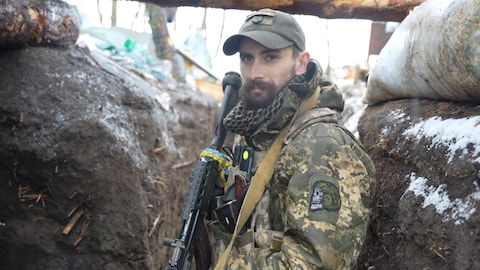 Un homme se tient dans une tranchée avec sa mitraillette en Ukraine.