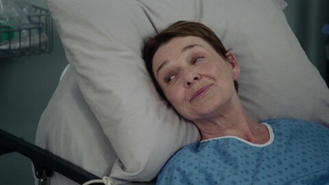 Édith est couchée dans un lit d'hôpital et regarde la personne à côté d'elle.
