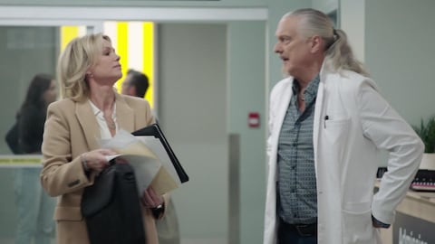 Pascal et Claude discutent dans un corridor de l'hôpital.