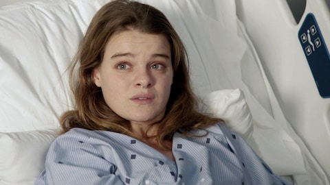Rosalie est couchée dans un lit d'hôpital et regarde une personne devant elle.
