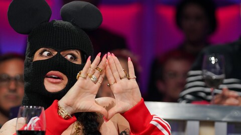 A. Media Elle est assise en studio avec sa cagoule noire.