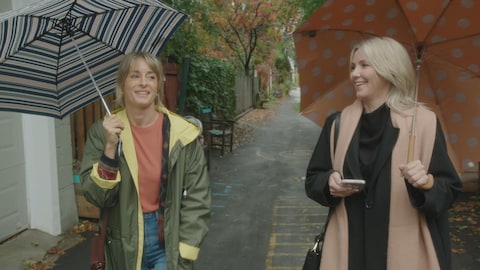 Photo de tournage dans une ruelle. Les deux comédiennes marchent avec des parapluies.