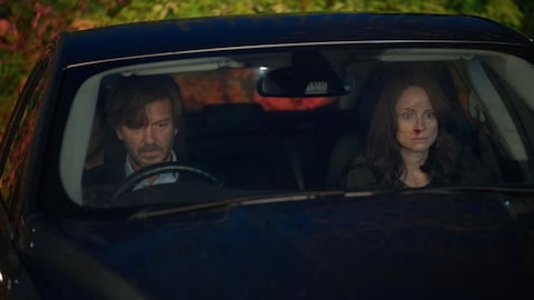 Un homme et une femme, le visage ensanglanté, sont assis dans une voiture. 