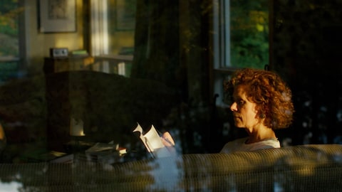 Catherine Perrin lit un livre dans un divan.