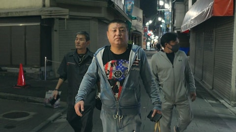 Des japonais marchent dans une rue sombre.