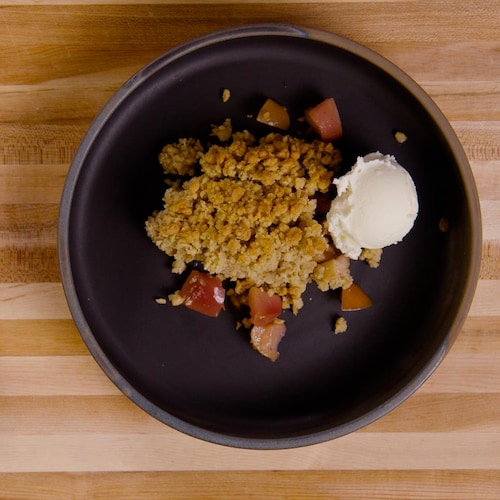 Sur une table, une assiette ronde contient une portion de croustade aux pommes et une boule de crème glacée vanille. 
