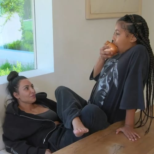 Kim Kardashian, assise, regarde sa fille North croquer dans un oignon jaune cru.