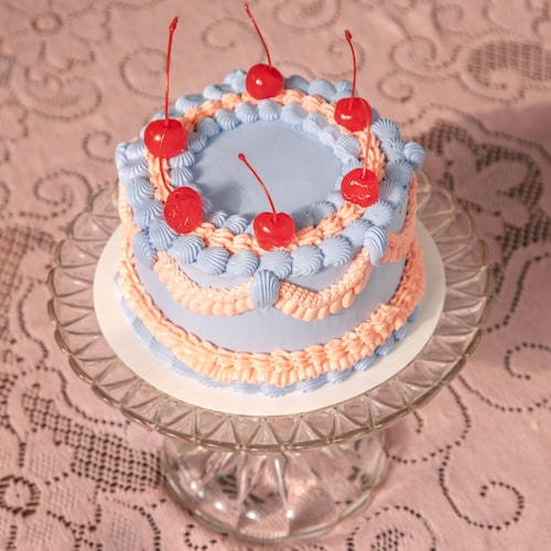 Un gâteau aux allures rétro décoré de cerises au marasquin sur une nappe blanche de dentelle. 