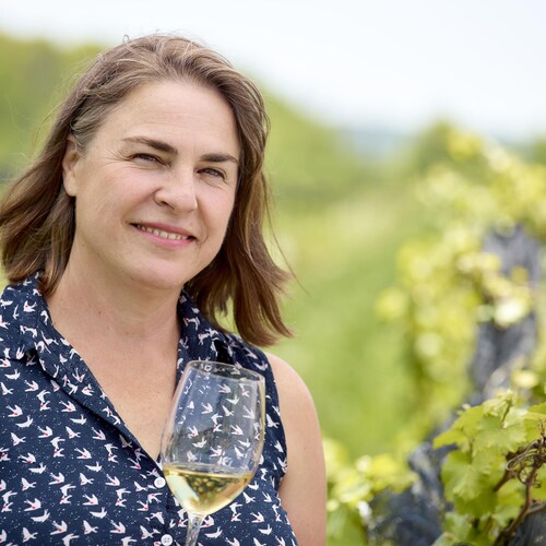 La vigneronne Ann Sperling dans son vignoble, un verre de vin blanc à la main.
