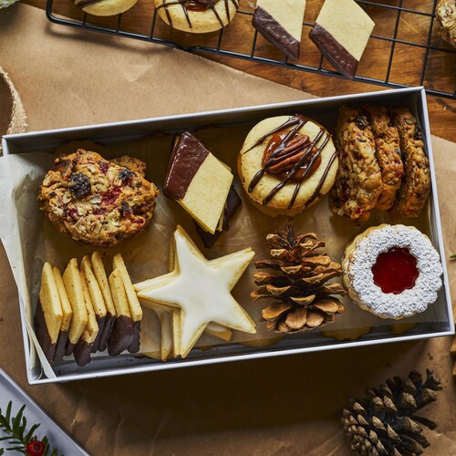 Une variété de biscuits de Noël disposés dans une boîte blanche entourée de rubans et de décorations de Noël. 