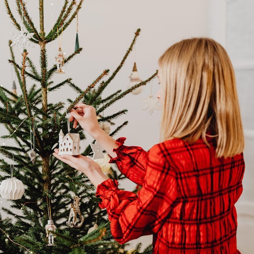 Une femme accroche une décoration de Noël dans un sapin.