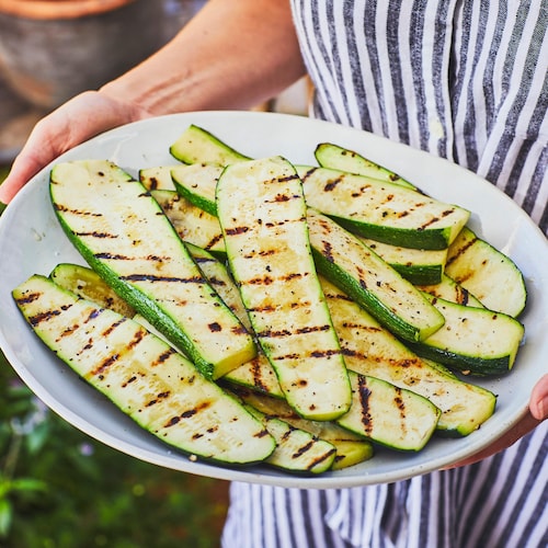 Une personne tient une grande assiette de service contenant des courgettes grillées. 