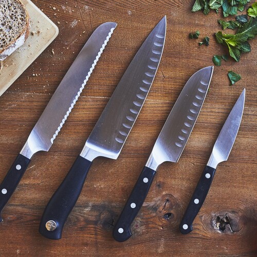 Quatre couteaux avec des tailles et des lames différentes sur un plan de travail en bois.