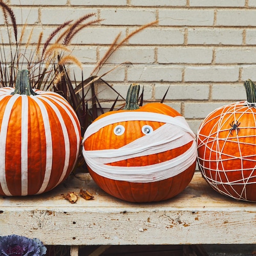 Trois citrouilles décorées pour l'Halloween sur un banc de bois.