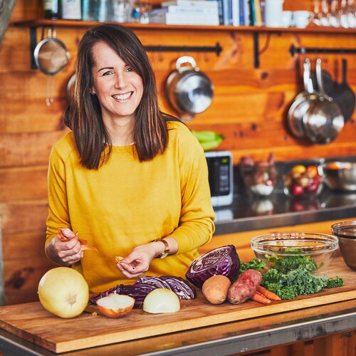 Geneviève O'Gleman dans la cuisine d'un chalet, manipule des légumes sur un ilot en bois. 