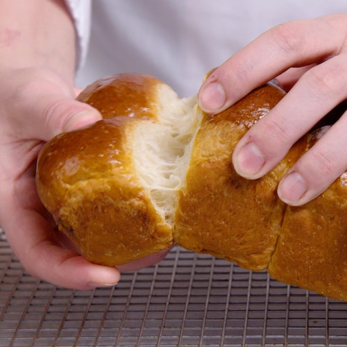 Des mains qui tiennent une miche de pain brioché.
