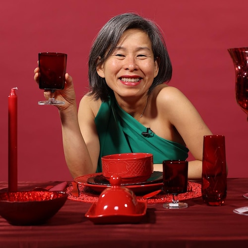 Kim Thúy assise à une table avec plusieurs verres, assiettes et bols rouges.