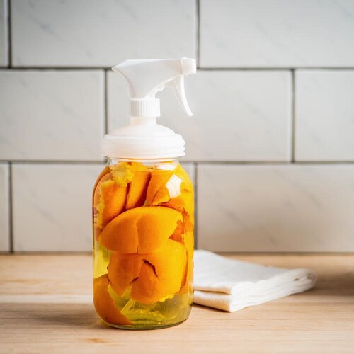Bouteille vaporisateur transparente contenant du vinaigre et des écorces d'oranges.