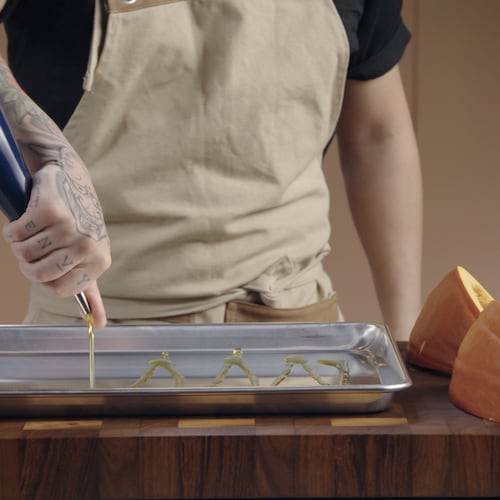 Une personne verse de l'huile d'olive sur une plaque de cuisson. 