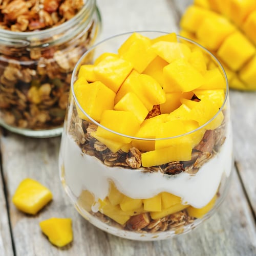 Une verrine remplie de yogourt, de céréales et d'une mangue coupée en morceaux.