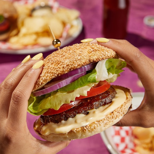 Un burger garni d'oignons rouges, de laitue, de tomates, de viande et d'une sauce blanche.