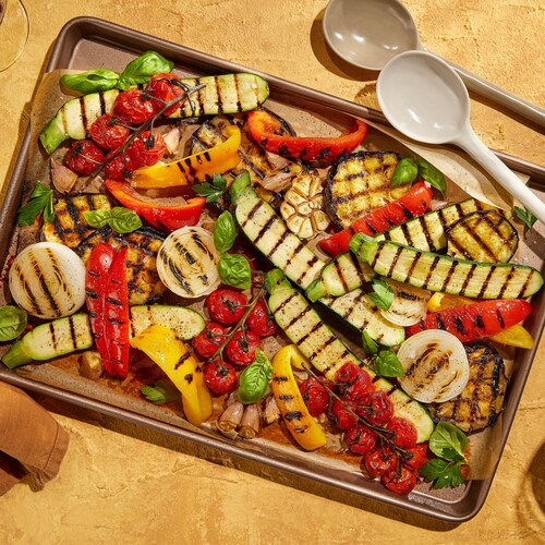 Une plaque de courgettes, de poivrons rouges et jaunes, de tomates en grappe et d'oignons grillés.