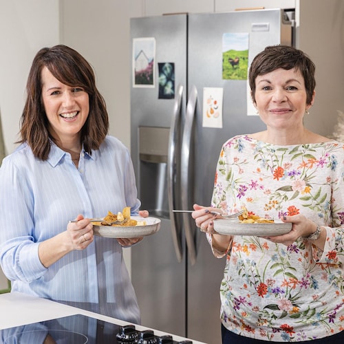 La nutritionniste Geneviève O’Gleman et la docteure en nutrition Karine Gravel sont dans une cuisine et tiennent chacune une assiette de poutine.