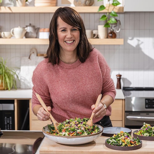 La nutritionniste Genviève O'Gleman se tient debout dans une cuisine et portionne une salade dans trois assiettes.