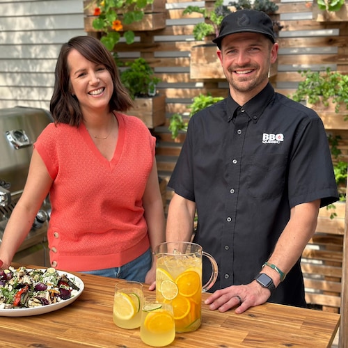 La nutritionniste Geneviève O’Gleman et le président de BBQ Québec, Max Lavoie, sont sur une terrasse à côté d’un barbecue et d’une table avec une agua fresca aux agrumes et un plat de poulet et légumes grillés à la grecque. 