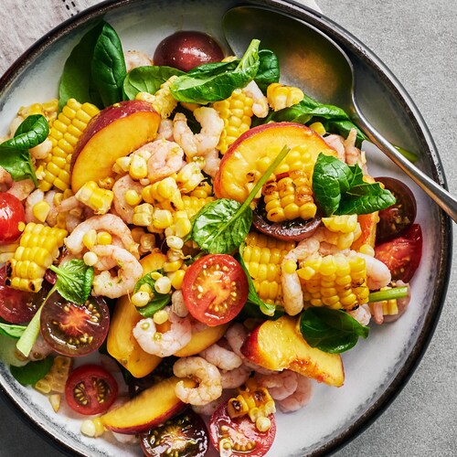 Une salade de maïs grillé, de pêches et de crevettes dans une assiette.