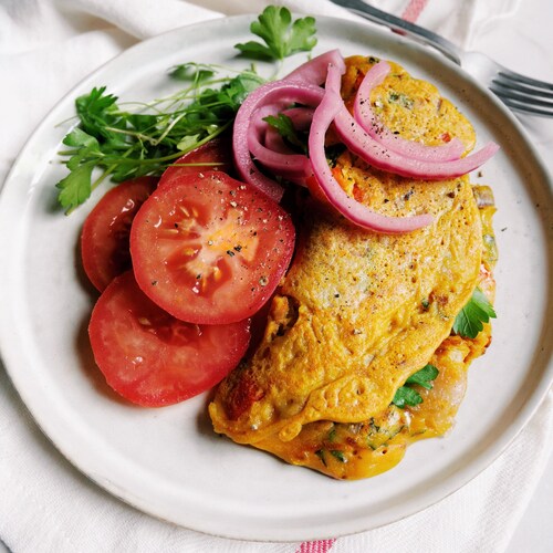 Une omelette aux légumes entourée de tranches de tomates et d'oignons et de persil dans une assiette.