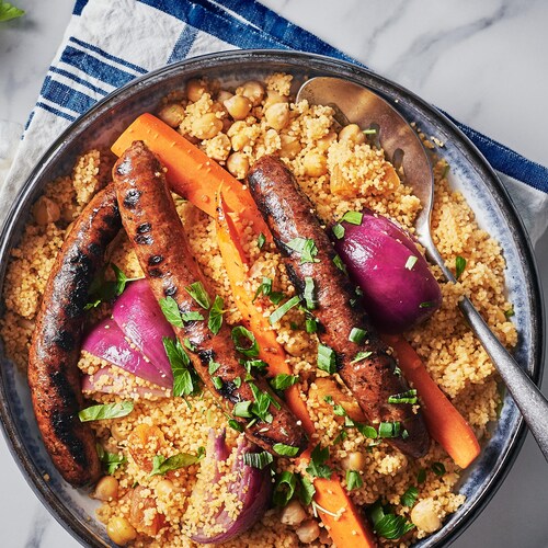 Un couscous garni de carottes, d'oignons et de merguez dans un plat.