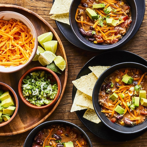 Plusieurs bols de soupe tacos avec ses options de garnitures : fromage, avocat, lime, chips.