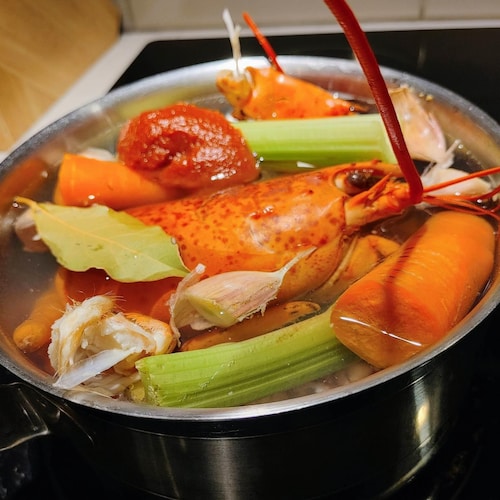 Une casserole contenant des carcasses de homard, des carottes, du céleri et des aromates.