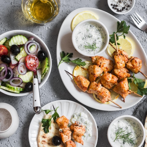 Une assiette de souvlakis de poulet, de la sauce tzatziki, de la salade grecque et des pitas.