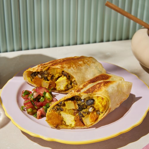 Un burrito déjeuner végétalien coupé en deux dans une assiette.